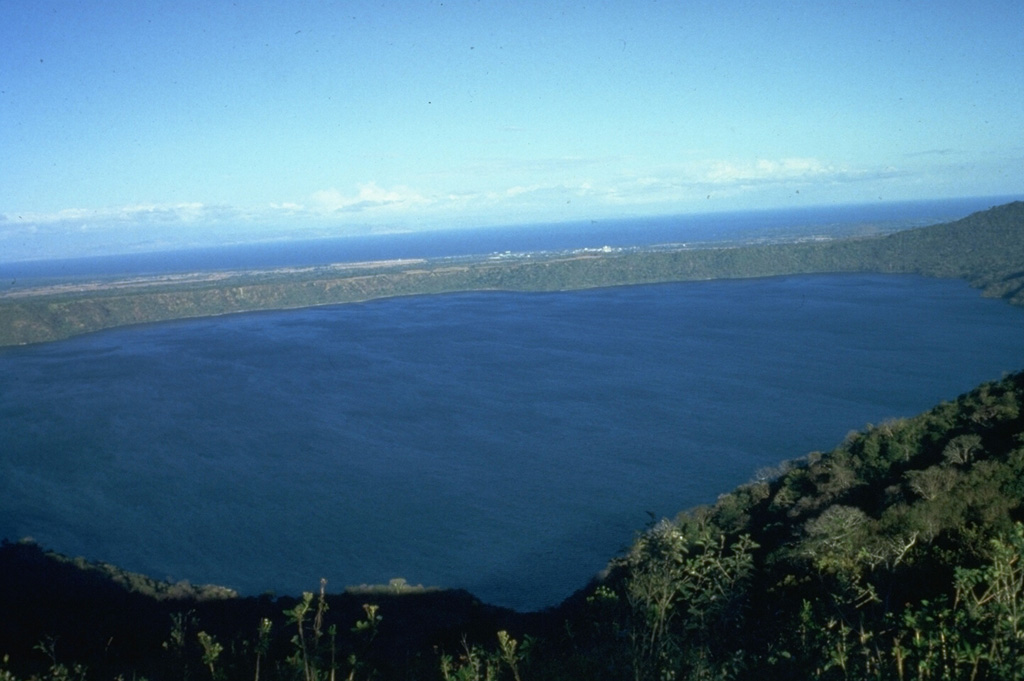 The 7-km-wide, lake-filled Apoyo caldera is seen here from the W with Lake Nicaragua in the distance beyond its low eastern caldera rim. The surface of Laguna de Apoyo is 78 m above sea level. The steep caldera walls rise about 100 m along the eastern rim and up to 500 m along the western rim (foreground). The caldera was formed during two major dacitic explosive eruptions radiocarbon dated at about 23,000 years BP. Photo by Jaime Incer.