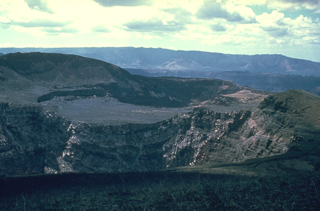 Three Masaya summit craters are visible in this view to the NW; Santiago crater appears in the foreground, with the flat, high surface of Nindirí crater in the middle and San Pedro crater behind it.  The flat-lying, lighter-colored lavas in the center are a part of a lava lake emplaced in Nindirí crater during an eruption in July 1852.  A small lava flow was also emitted at that time, a few years before the formation of Santiago and San Pedro pit craters in 1858-1859. The NW wall of Masaya caldera forms the low ridge in the middle distance. Photo by Dick Stoiber, 1963 (Dartmouth College).