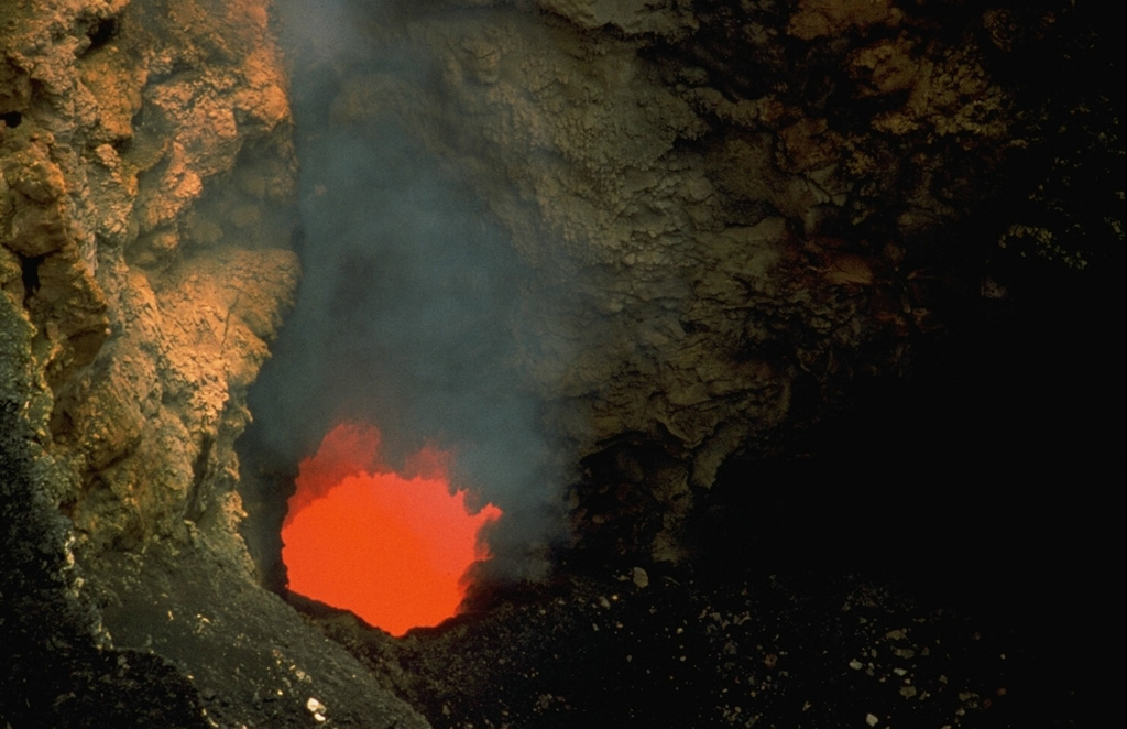 An incandescent vent glows on the floor of Santiago crater in July 1972.  A new lava lake formed in Santiago crater in October 1965.  By 1969 activity was restricted to a small spatter cone; after it collapsed in 1972 a lava lake was visible until 1979.  Periodic lava lake activity has occurred since the time of the Spanish Conquistadors.  The partially yellow incandescence of the active lava lake was taken for molten gold, prompting several attempts to mine it. Photo by Dick Stoiber, 1972 (Dartmouth College).