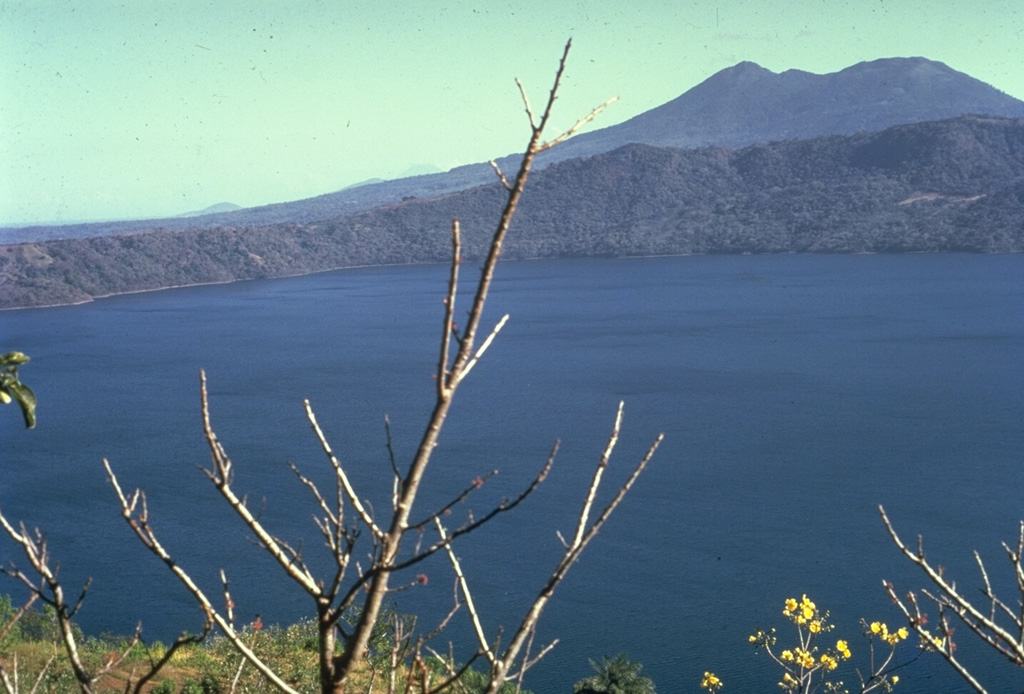 The 7-km-wide, lake-filled Apoyo caldera, seen here from the NW with Mombacho volcano in the background, is a large silicic volcanic center immediately SE of Masaya caldera.  An early shield volcano constructed of basaltic-to-andesitic lava flows and small rhyodacitic lava domes collapsed following two major dacitic explosive eruptions about 23,000 years ago.  Post-caldera ring-fracture eruptions formed the Granada cinder cones and La Joya collapse craters along fracture systems to the east of the caldera.  The age of the latest activity is not known. Photo by Alain Creusot-Eon, courtesy of Jaime Incer, 1968.