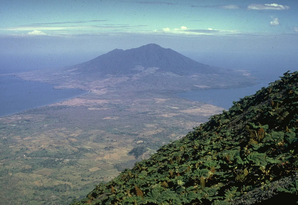 Volcán Maderas is a symmetrical, 1394-m-high stratovolcano that forms the SE end of the dumbbell-shaped Ometepe island in Lake Nicaragua.  It is seen here from the upper slopes of Concepción volcano, to which it is connected by a narrow isthmus.  Maderas is cut by numerous faults and small grabens.  Many pyroclastic cones are situated on the lower NE flank down at the level of Lake Nicaragua.  The latest period of major growth of the volcano took place more than 3000 years ago. Photo by Alain Creuset-Eon, 1972 (courtesy of Jaime Incer).