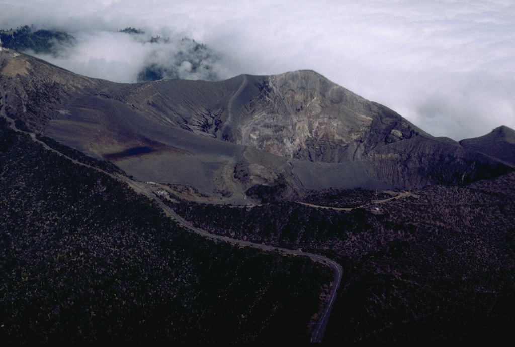 This view of Irazú from the SE shows the road leading to the summit (upper left) and principal crater (right center). The road winds 32 km up the flanks to the summit crater complex, a tourist attraction near the capital city of San José. The roughly 200-m-deep summit crater has been the source of most historical eruptions. Photo by William Melson, 1986 (Smithsonian Institution).