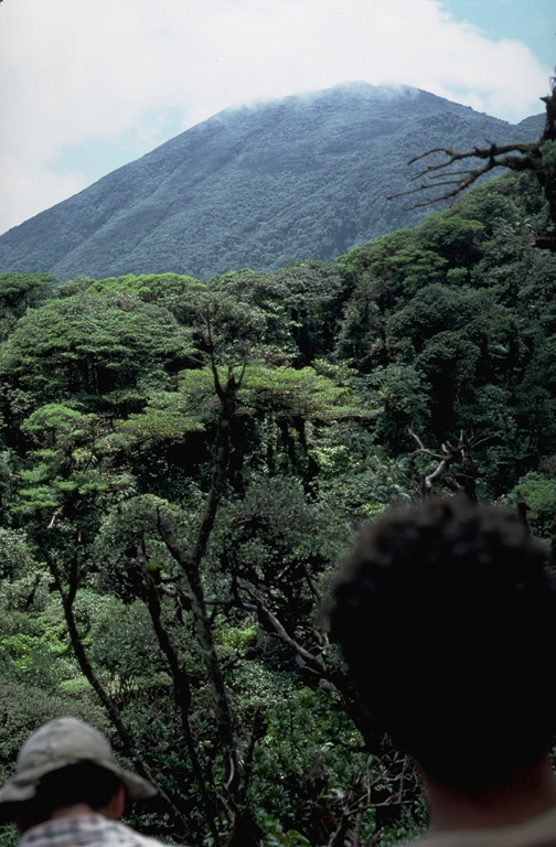 The verdant forests mantling the Tenorio volcanic complex are seen from the Río Celeste drainage.  The Tenorio complex consists of five volcanic cones aligned NNW-SSE.  Several archaeological sites are located around the complex, testament to the importance of the area to prehispanic Indians.  The Tenorio complex marks the SE end of the Guanacaste Range; a range of low hills separates it from the next volcano to the SE, Arenal. Photo by William Melson, 1985 (Smithsonian Institution).