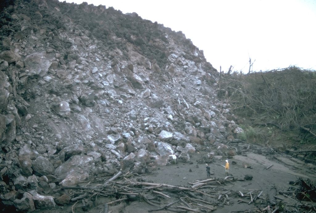 Geologists stand in front of a steep lava flow margin in the Río Tabacón. Lava emission began on 19 September 1968, and in October the flow was advancing at rates of 10-30 m/day. By the time of this photo in November 1968 it had reached about 2.5 km from its source on the western flank. This area has now been buried by younger flows. Photo by William Melson, 1968 (Smithsonian Institution).
