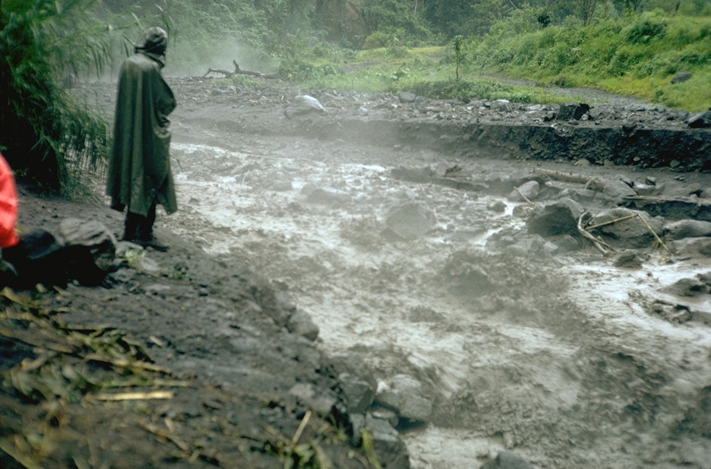 Steam rises from of a small, hot lahar as it travels down the Río Tabacón on the NW flank of Arenal in August 1968, following a powerful explosive eruption that began on 29 July. The lahar damaged the road across the base of the volcano, about 4 km from the summit.  Photo by William Melson, 1968 (Smithsonian Institution).