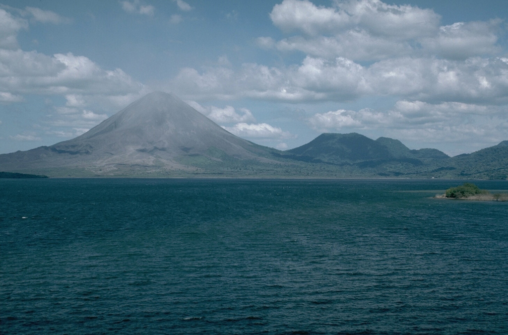 The Arenal volcanic complex, seen here in 1990 from Lake Arenal to its SW, consists of the Arenal edifice (left) and the older Cerro Chato (right), whose flat summit contains a crater and a crater lake. Activity at the complex has migrated to the NW from the Chatito and La Espina lava domes to the right of Cerro Chato.  Photo by William Melson, 1990 (Smithsonian Institution)