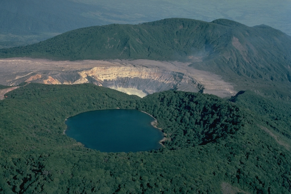 The summit of Poás volcano, seen here in 1983 from the south, contains a group of craters along a N-S line.  The forested Botos cone (foreground) is filled with the waters of Laguna del Agua Fría (also known as Laguna del Poás).  The unvegetated active summit crater appears at the center.  A third crater cuts the south side of the forested von Frantzius cone in the background. Copyrighted photo by Katia and Maurice Krafft, 1983.