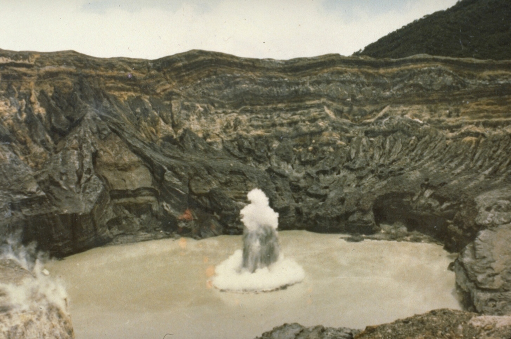 An ejection of steam and ash rises above the surface of the crater lake of Poás volcano in July 1977. The white ring at the base of the eruption plume is a steam cloud that is traveling along the surface of the lake. Mild phreatic explosions such as this one were typical of the eruption that began in May 1977 and lasted at least until July. The crater walls rise about 250 m above the lake. Photo by S. Racchini, 1977 (Universidad Nacional Costa Rica, courtesy of Jorge Barquero).