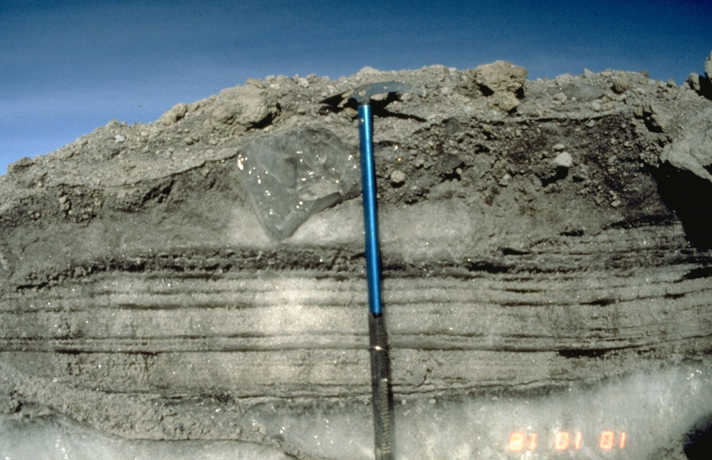 A record of the 13 November 1985 eruption of Nevado de Ruiz was preserved in ice-rich levees of pyroclastic flows. This photo, taken a month later, shows parallel-bedded pyroclastic-surge deposits, composed of snow grains and tephra, which were deposited over a pre-existing ice at the bottom of the photo. The surge layers are overlain at the top by coarser-grained pyroclastic-flow deposits. The clast of glacial ice (located left of the upper part of the ice axe) was scoured and incorporated into the pyroclastic flow. Photo by Tom Pierson, 1985 (U.S. Geological Survey).