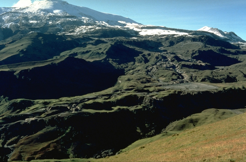 On 13 November 1985 lahars traveled down the upper Guali River drainage on the N flank of Nevado del Ruiz, seen here descending diagonally from right of center to the lower left. Farmhouses are visible on the opposite side of the channel for scale. The lahars traveled down the Río Guali at velocities up to 17 meters/second to over 100 km from the volcano. Photo by Tom Pierson, 1985 (U.S. Geological Survey).
