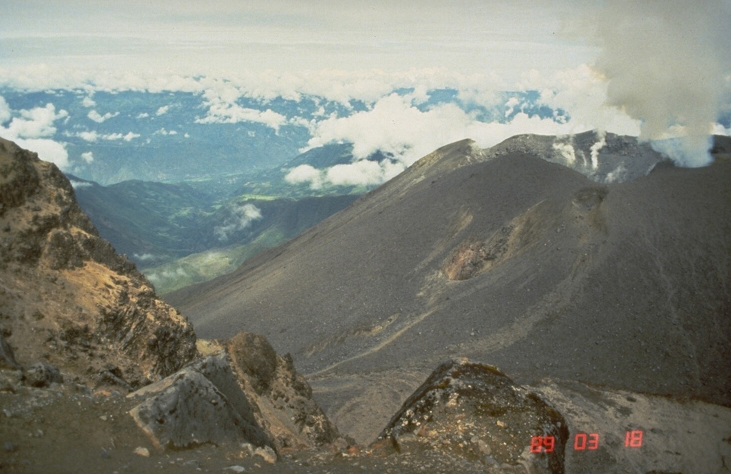A large cone fills much of the large collapse scar at Galeras. It is seen degassing here on 18 March 1989 from the SE. The El Viejo flank crater can be seen near the center of the photo, with the Bastón fissure to the right, just below the rim of the main crater. The central cone has been the site of frequent eruptions since the time of the Spanish conquistadors. Photo by Norm Banks, 1989 (U.S. Geological Survey).
