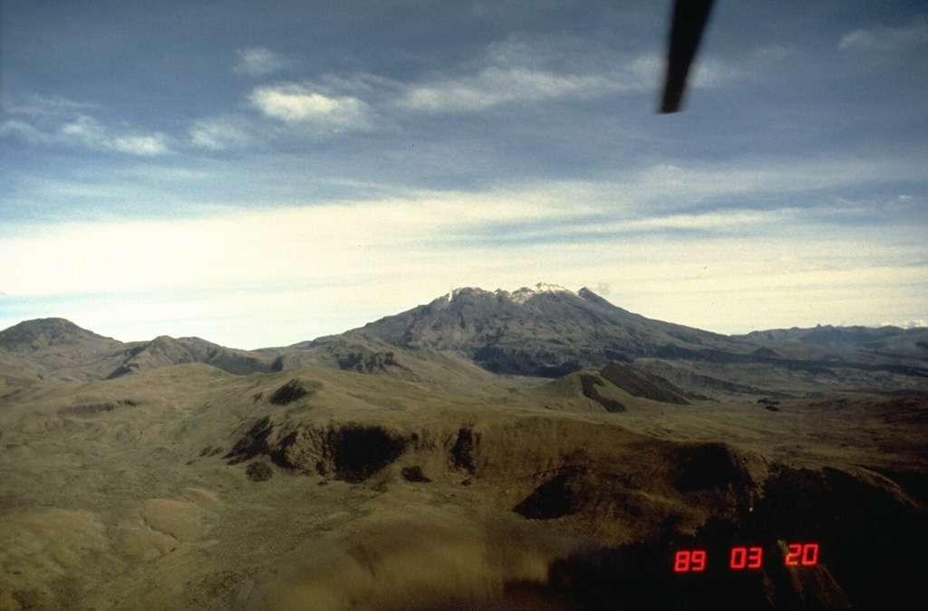 Azufral stratovolcano in southern Colombia, seen here from the SE, is also known as Azufral de Túquerres.  It is truncated by a 2.5 x 3 km caldera containing a Holocene lava dome complex.  A crescent-shaped lake, Laguna Verde, occupies the NW side of the caldera.  Nearly a dozen lava domes are present, the latest of which were formed about 3600 years ago and have active fumaroles.  The last known eruption of Azufral volcano took place about 1000 years ago.     Photo by Norm Banks, 1989 (U.S. Geological Survey).