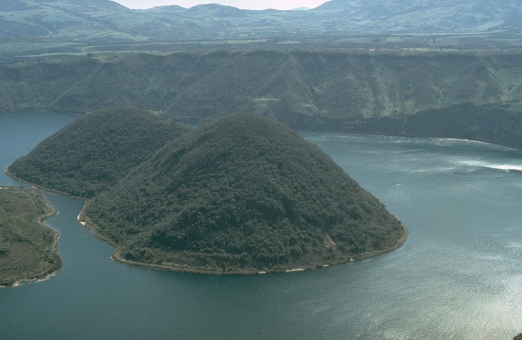 An explosive eruption about 2900 years ago produced widespread tephra and pyroclastic surges.  Subsequently a group of four dacitic lava domes was constructed within Cuicocha caldera.  This marks the latest known activity from the caldera.  The eastern two domes are seen here from the SE rim of the caldera.  The lava domes form two forested islands in the center of the 3-km-wide caldera. Photo by Tom Pierson, 1992 (U.S. Geological Survey).