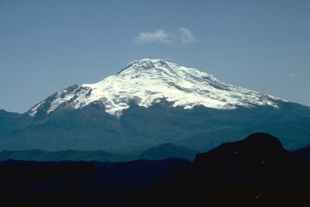 The massive compound Cayambe stratovolcano, seen here from the SW across Ecuador's Interandean Depression, is the northernmost of a chain of  large, glacier-covered Holocene volcanoes along the western edge of the Cordillera Real.  No historical eruptions are known from 5790-m-high Cayambe, although lava flows on the flanks of the volcano have very young morphologies.  Pyroclastic-flow deposits of possible Holocene age are present. Photo by Minard Hall, 1982 (Escuela Politécnica Nacional, Quito).