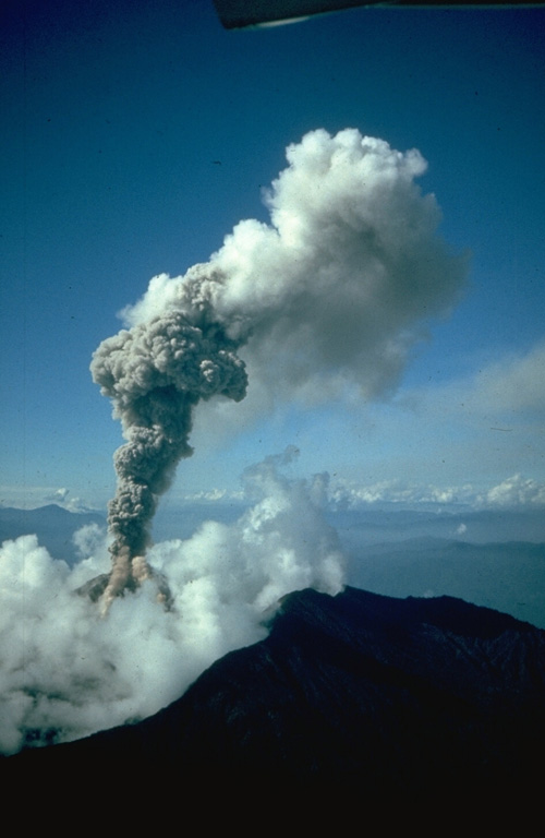 An ash column rises above the summit crater of Reventador volcano during the 1976 eruption.  This view across the north caldera rim in the foreground shows a small pyroclastic flow descending the flank of the summit cone into the clouds.  Pyroclastic flows began between the 2nd and 3rd weeks of the eruption, which started on January 1.  They originated from collapse of the vertical eruption column and traveled down the flanks of the volcano onto the floor of the breached caldera.  Pyroclastic-flow activity continued for several months. Photo by Minard Hall, 1976 (Escuela Politécnica Nacional, Quito).