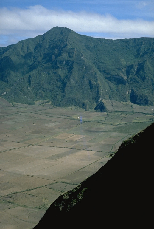 The flat floor of the 3-km-wide caldera of Pululagua volcano is used for agricultural purposes.  This view from the SE caldera rim looks across to Loma El Lavadero on the NE rim, 700 m above the caldera floor.  Pululagua's caldera was formed during major explosive eruptions about 2400 years ago that produced plinian airfall deposits, pyroclastic flows, and pyroclastic surges. Photo by Lee Siebert, 1978 (Smithsonian Institution).