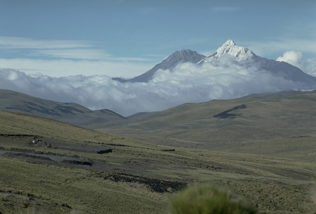 The twin peaks of Illiniza volcano form prominent landmarks west of the Interandean Valley.  Sharp-peaked, snow-covered Illiniza Sur (right) is the higher of the two peaks.  It is seen here from the south with Illiniza Norte to its left.  Illiniza is largely, if not entirely Pleistocene in age.  However, Rasuyacu lava dome on the south flank was active during the Holocene.  Recent work suggests that Illiniza itself, which is substantially eroded, may have had relatively young eruptions. Photo by Lee Siebert, 1978 (Smithsonian Institution).