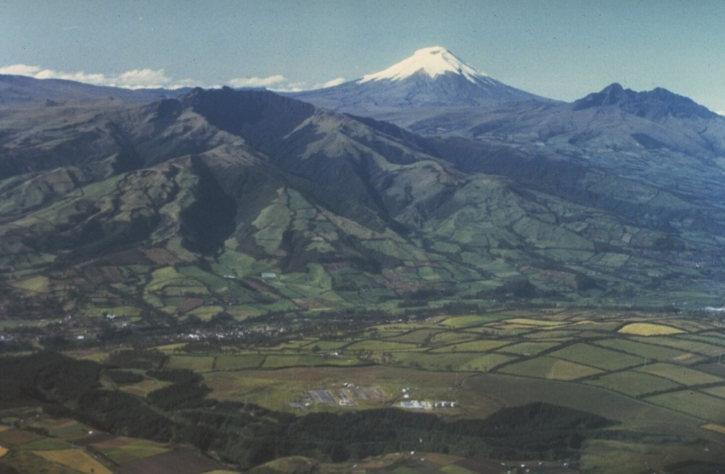 Snow-capped Cotopaxi volcano towers above the Interandean valley, forming one of Ecuador's most familiar landmarks.  The older Pleistocene volcanoes of Pasochoa (left center) and Rumiñahui (extreme right) appear in the foreground of this aerial view from the NW.  Cotopaxi is one of Ecuador's most active volcanoes, having erupted more than 50 times since the 16th century. Photo by Minard Hall, 1980 (Escuela Politécnica Nacional, Quito).