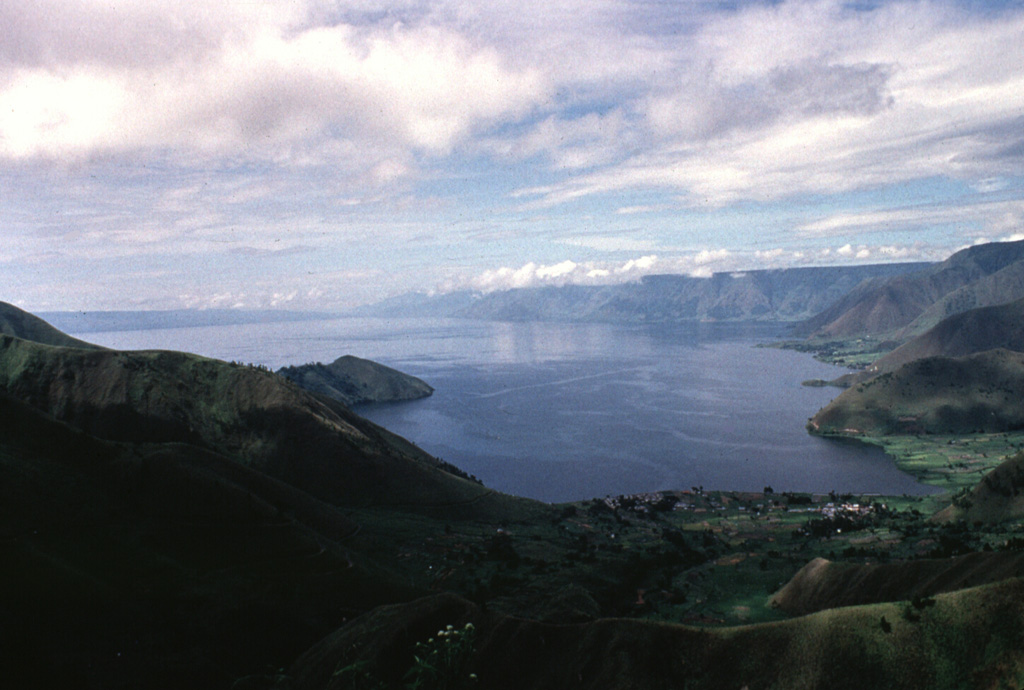 The 100-km-long Lake Toba is seen here from the northern end. The lake fills a 35 x 100 km caldera that formed during four major late-Pleistocene eruptions. The western caldera scarp forms the cliffs at the right. The low-angle slope on the left horizon is Samosir Island, half of a large resurgent block in the center of the caldera. The 1,700 km2 lake is the largest in SE Asia. Anonymous, 1993.