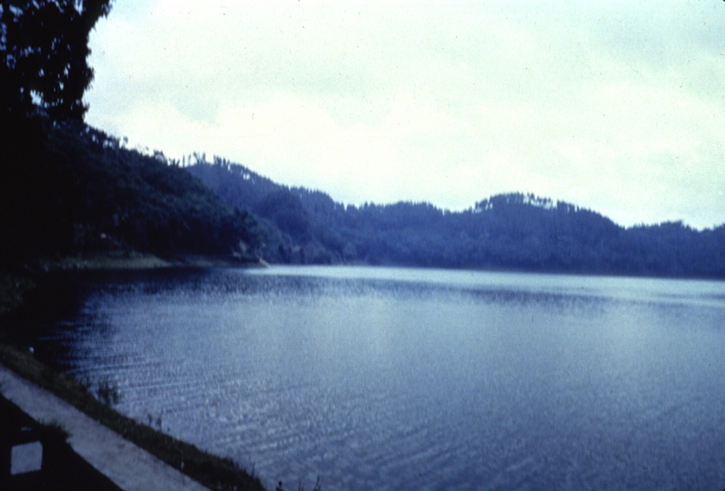 Lake Ngebel is located on the lower western flank of Gunung Wilis and displays fumaroles and mud pots. The lake is viewed here from its SSE shore. Wilis is a volcanic massif surrounded by low-elevation plains on all but its southern side. It was formed during three episodes dating back to the mid Pleistocene and the most recent cone grew during the Holocene.  Anonymous, 1987.