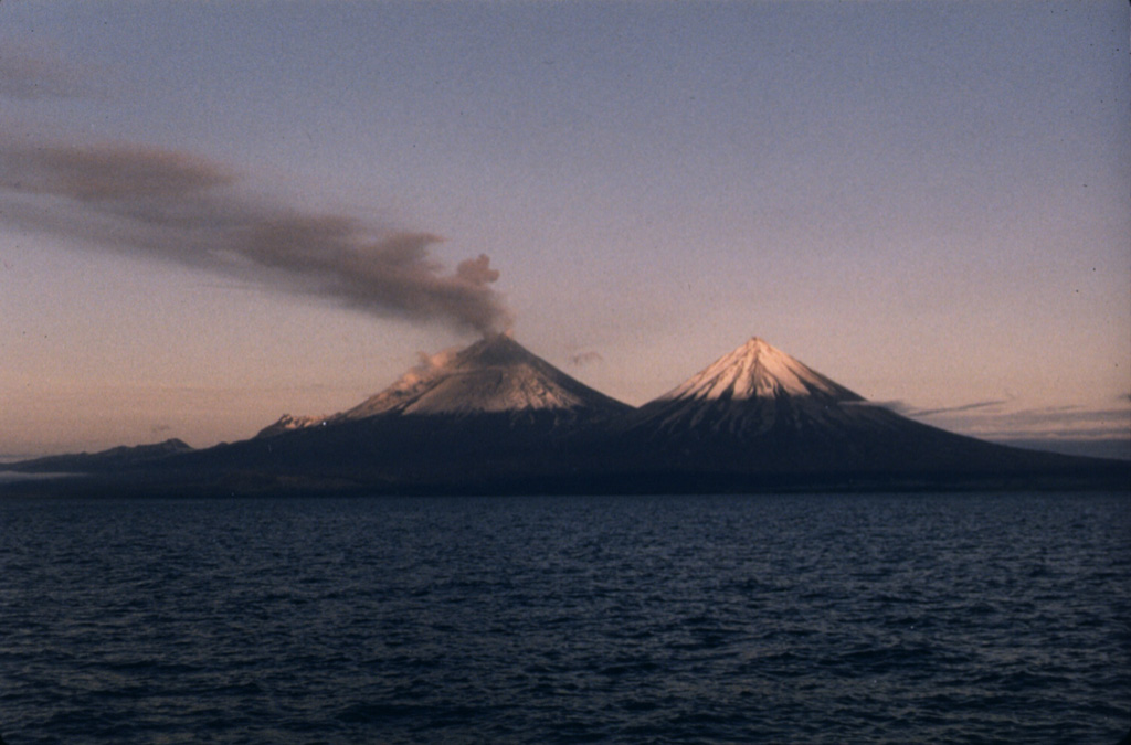 An ash plume disperses to the south in mid-July 1986, three months after the start of an eruption of Pavlof that lasted nearly 2.5 years. This photo was taken from the west on a fishing boat in Pavlof Bay, with Pavlof Sister to the right. The 1986-88 eruption produced intermittent ashfall and lava flows from two vents near the summit, one halfway down the SE flank, and another 600 m below the summit on the NE flank. Lava flows traveled to the N, NE, SE, ESE, and SSE, the latter to within 600 m of the Pavlof Bay shoreline. Photo by Richard Mack, 1986.