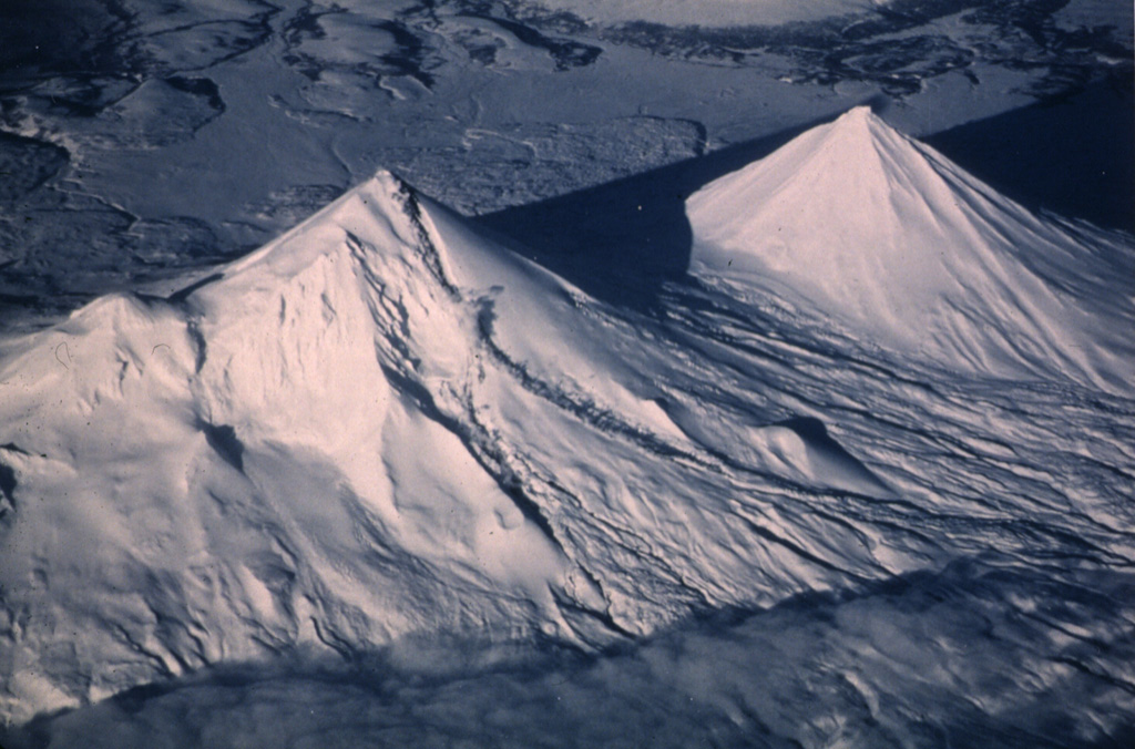 Pavlof (left) and Pavlof Sister (right) are shown in this 20 January 1987 view from the SW. Small steam plumes rise along the length of a lava flow descending a valley on the SE (right) flank of Pavlof. Recent snowfall covers ashfall that was frequently deposited on its slopes. This eruption began with explosive activity on 16 April 1986 and continued until 13 August 1988. Lava flows traveled down the N, NE, SE, ESE, and SSE flanks, the latter reaching to within 600 m of Pavlof Bay. Photo by Jerry Chisum (Mark Air), 1987 (courtesy of John Reeder, Alaska Div. Geology Geophysical Surveys).