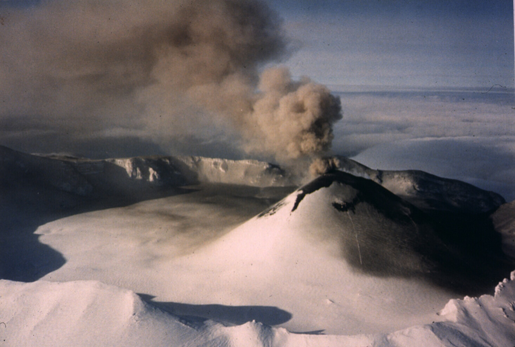 Intermittent explosive eruptions took place from the scoria cone in Akutan caldera during 31 January-2 March and 22-24 June 1987. This 11 February photo from the SE shows an ash plume rising from a crater at the top of the cone. Ash was deposited across the cone flank and the N side of the caldera floor. Photo by Jerry Chisum (Mark Airways), 1987 (courtesy of John Reeder, Alaska Div. Geology & Geophysical Surveys).
