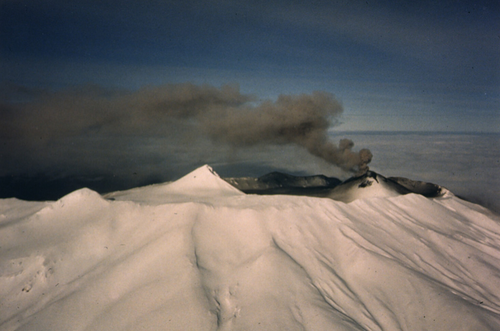 Akutan has a 2-km-wide summit caldera with a large scoria cone that rises above the caldera rim. It is seen here from the south in eruption on 11 February 1987. A small lake occupies part of the caldera floor. The caldera rim is breached narrowly on the north side through which a 1978 lava flow traveled to within 2 km of the sea. Photo by Jerry Chisum (Mark Airways), 1987 (courtesy of John Reeder, Alaska Div. Geology & Geophysical Surveys).