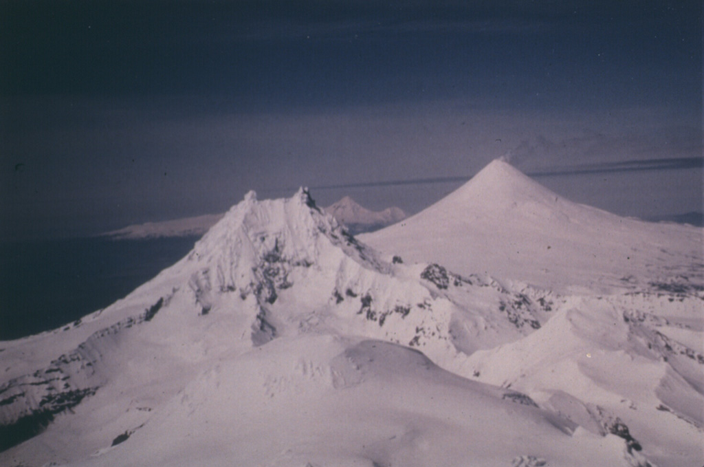 Three volcanoes are constructed along an E-W trend on the eastern half of Unimak Island. Roundtop in the foreground is glacially eroded and has Holocene pyroclastic flow deposits and a group of lava domes to the south. Isanotski is in the background and Shishaldin is in the midground. Photo by Clayton and Marcia Brown, 1986 (courtesy of John Reeder, Alaska Div. Geology Geophysical Surveys).