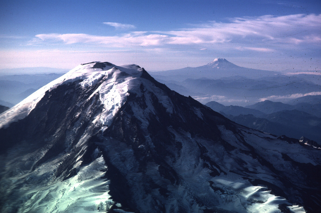 This view of Mount Rainier from the NW shows neighboring Mount Adams to the right in 1985. The steep Willis Wall, named after the 19th-century geologist Bailey Willis, is to the left and exposes relatively young lava flows.  Photo by Lee Siebert, 1985 (Smithsonian Institution)