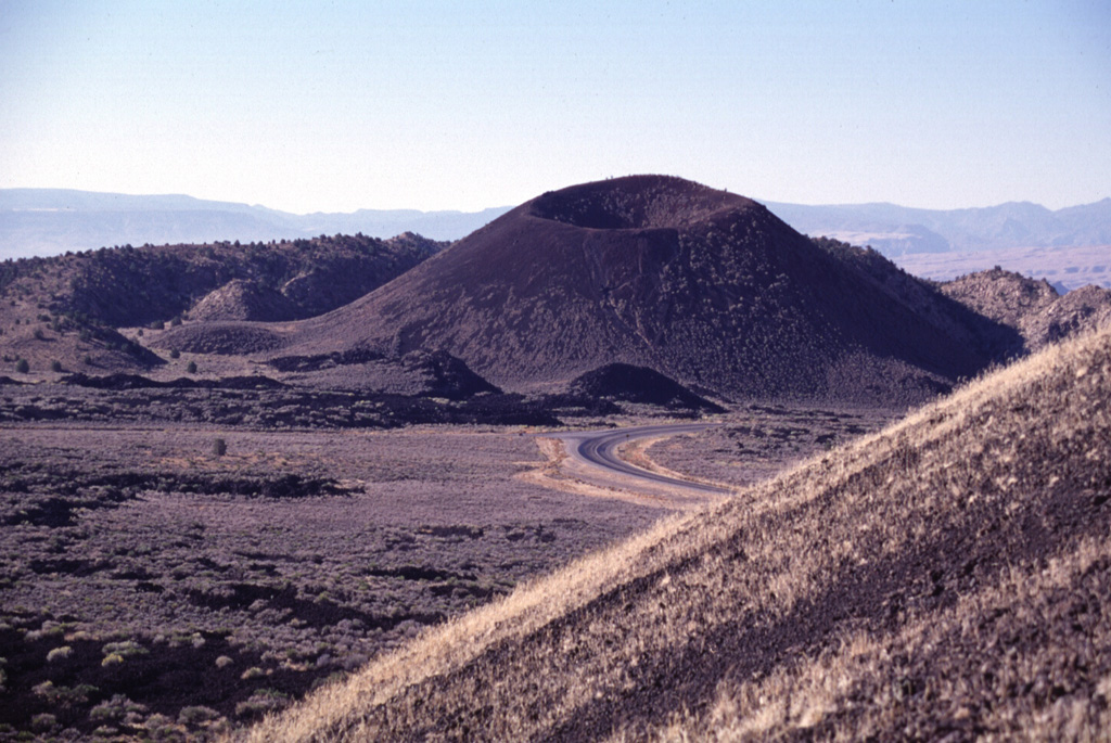 Two cinder cones in the Diamond Valley of SW Utah were the sources of the voluminous Santa Clara lava flow, one of the youngest in Utah.  The symmetrical southern cone, capped by a pristine crater, is seen here from the flanks of the northern cone.  Lava flows from the two cones filled the lower Diamond Valley in the foreground and then spilled through a narrow gap to the right of the southern cone into Snow Canyon. Photo by Lee Siebert, 1996 (Smithsonian Institution).