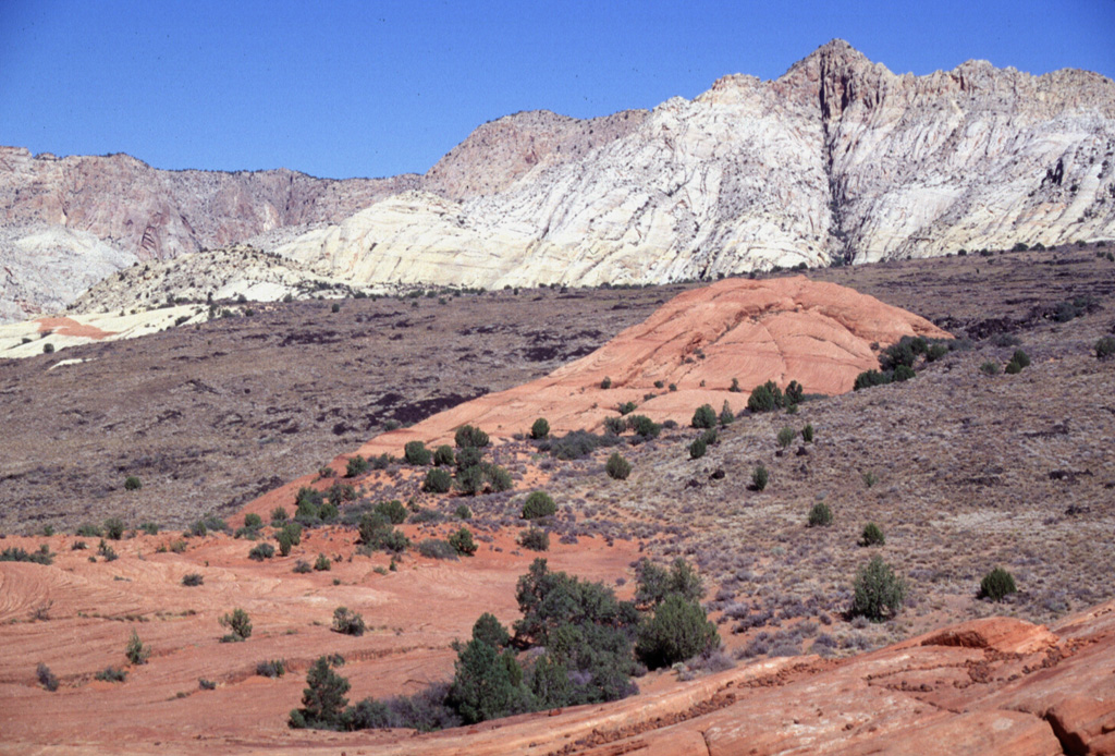 The sparsely vegetated Santa Clara lava flow traveled 16 km to the south down Snow Canyon, cut through the colorful red and white rocks of the Navajo Sandstone formation.  The flow, originating from two youthful cinder cones in Diamond Valley above Snow Canyon, was produced during one of the youngest eruptions in the Colorado Plateau/Basin and Range region.  This Pliocene-to-Quaternary volcanic field north of St. George in SW Utah contains numerous basaltic cinder cones and lava flows.  Photo by Lee Siebert, 1996 (Smithsonian Institution).