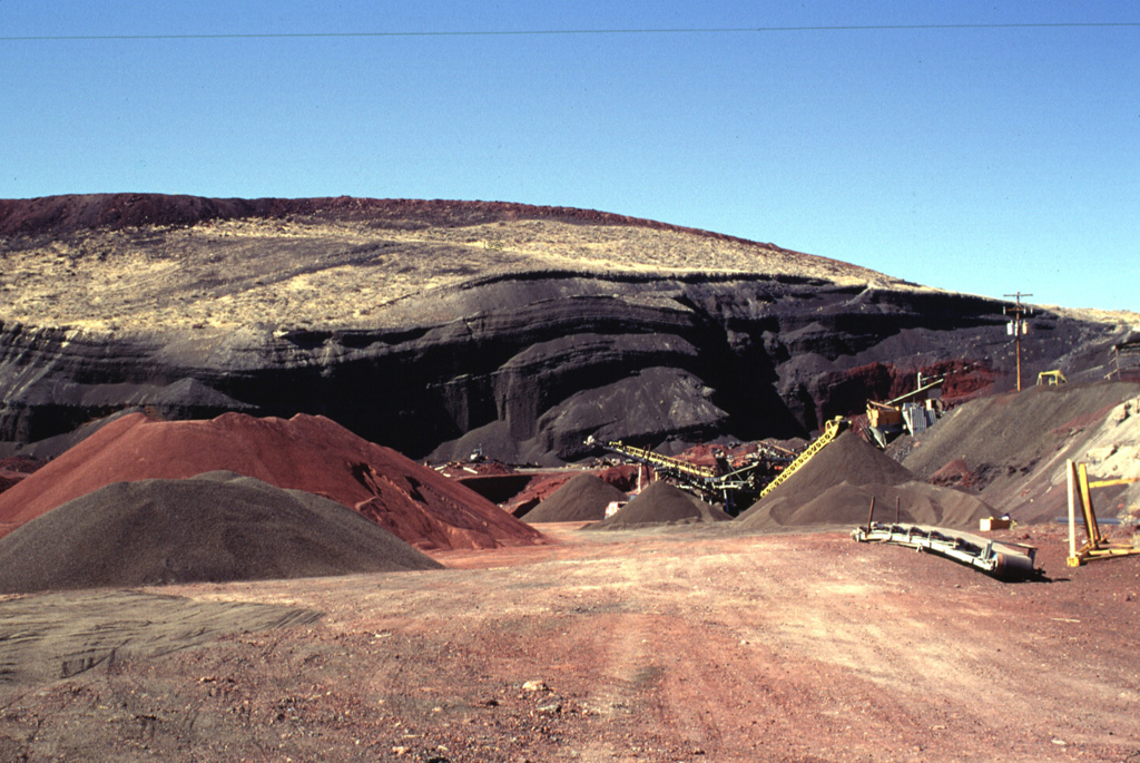 The multi-colored scoria deposits of the eastern side of Crescent Crater, part of the cinder and spatter cone complex at Ice Springs volcanic field, are the object of a mining operation to produce road aggregate.  Ice Springs was the source of Utah's youngest lava flow about 660 years ago.  Photo by Lee Siebert, 1996 (Smithsonian Institution).