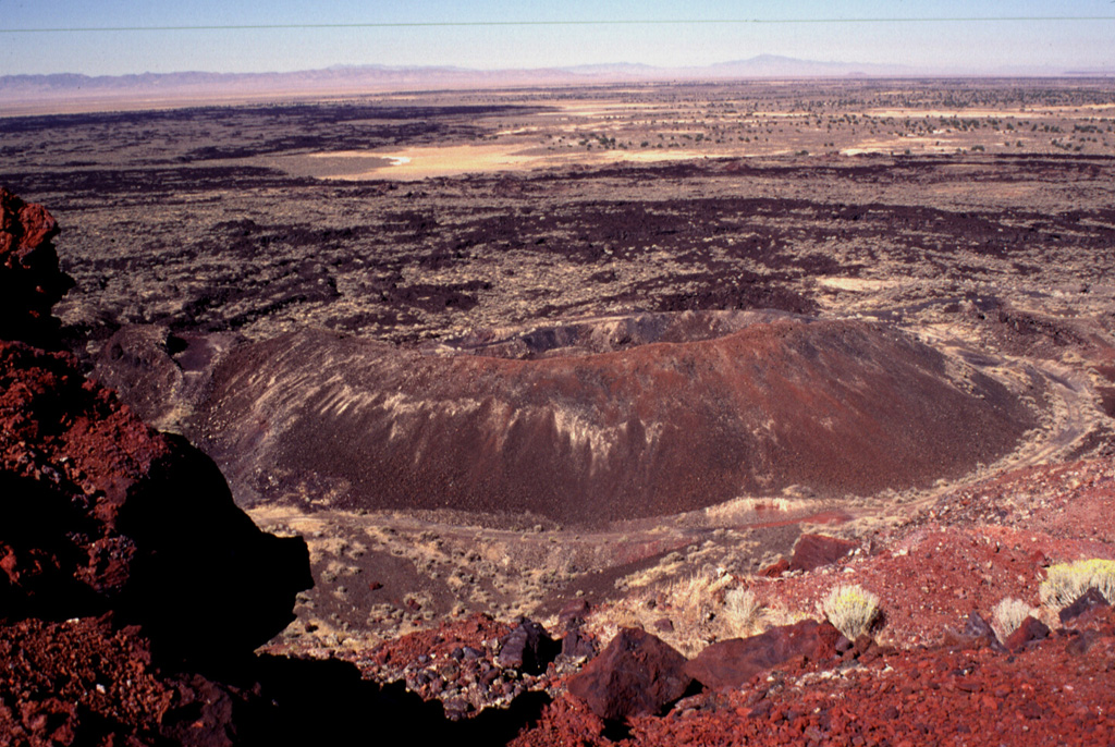 The youngest volcanic eruptions in Utah took place from the Ice Springs volcanic center.  Root fragments from soil beneath the lava flow are C-14 dated at 660 +/- 170 years old.  Lava flows from the Ice Springs crater complex traveled about 4 km to the west and north, overlapping late-Pleistocene flows from the Pavant volcano.  This view looks to the west from the rim of Crescent Crater, the largest of the overlapping cinder and spatter cones that fed the flows.  Pocket Crater is the symmetrical cone in the center of the photo.  Photo by Lee Siebert, 1996 (Smithsonian Institution).
