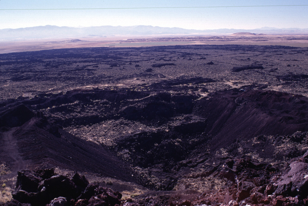 The Terrace, a crater seen here in the foreground from the rim of Mitre Crater, was the source of the voluminous lava flows seen extending toward the SE.  The crater derives its name from several terraces, now partly removed by quarrying operations, that were formed by cooled lava lakes.  These SE flows from The Terrace are the youngest of a series of eruptions at the Ice Springs volcanic field about 660 years ago.  The Ice Springs volcanic field is one of several closely spaced volcanic fields in the Black Rock Desert of south-central Utah. Photo by Lee Siebert, 1996 (Smithsonian Institution).