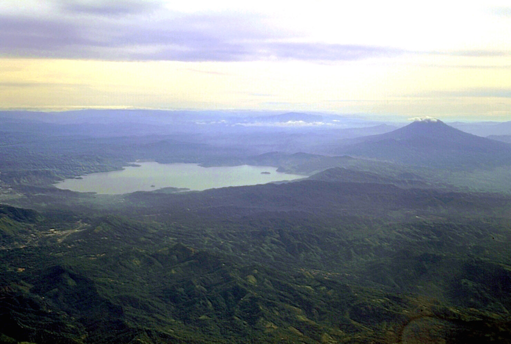 Ilopango caldera is seen in this aerial view from the SW with San Vicente stratovolcano to the right. The latest collapse of the 13 x 17 km caldera occurred after a powerful eruption during 536-550 CE that produced widespread pyroclastic flows and devastated early Mayan cities. The caldera now contains a lake with lava domes forming small islands near the shore and near its center. Copyrighted photo by Stephen O'Meara.