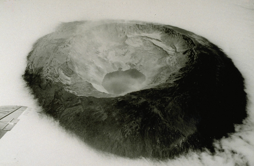 The 1968 eruption of Fernandina was one of the few historical instances in which caldera collapse has been documented.  This oblique aerial photograph taken three weeks after the start of the caldera collapse shows Fernandina volcano from the ESE.  The NW and SE benches and the central tuff cone (whose crater is partially filled by the small embayment at the top of the lake) can still be seen in this photograph, despite roughly 350 m subsidence of the SE caldera floor.  Note the dust from rock avalanches on the oversteepened walls.  Photo by U.S. Air Force, 1968 (published in Simkin and Howard, 1970).