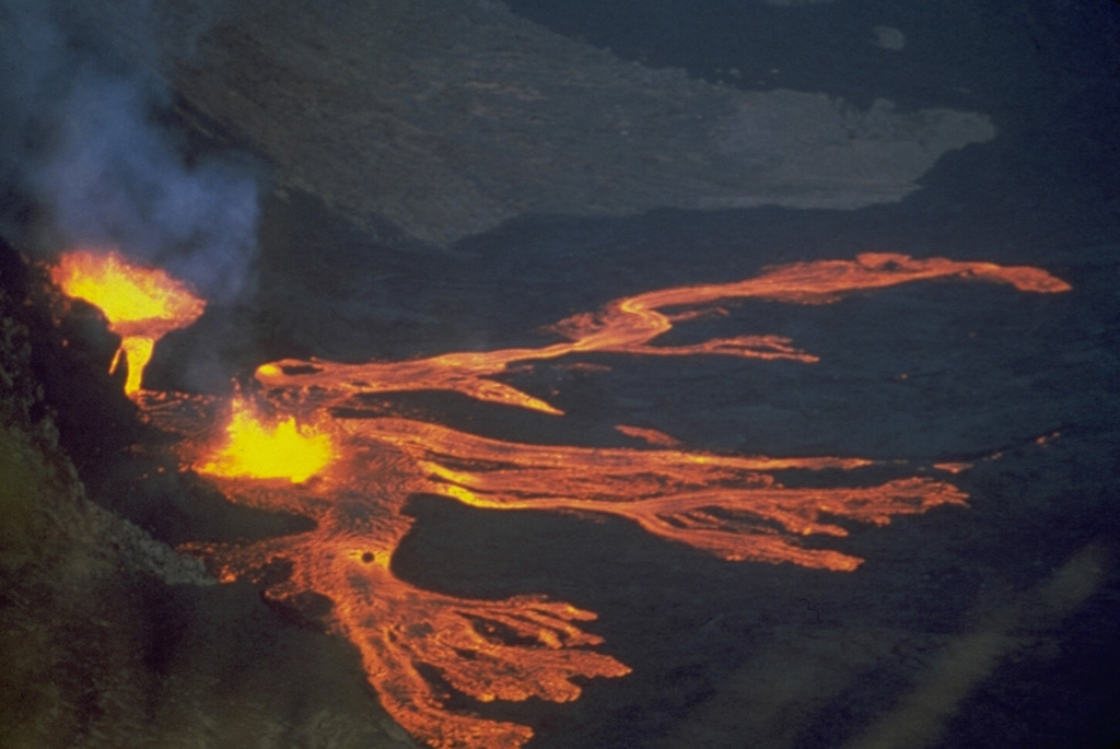 Lava fountains from Fernandina volcano in the Galápagos Islands feed multiple lobes of lava in 1978 that travel across a down-dropped block of the NW caldera bench, about 380 m below the caldera rim. The 1978 eruption began on 8 August when a 6-km-high eruption plume rose to be visible from distant locations in the archipelago. During the course of the eruption lava flows traveled 2 km into the caldera lake, more than 400 m below. Activity ended on 26 August. Photo by Marc Orbach, 1978 (courtesy of Tom Simkin, Smithsonian Institution).