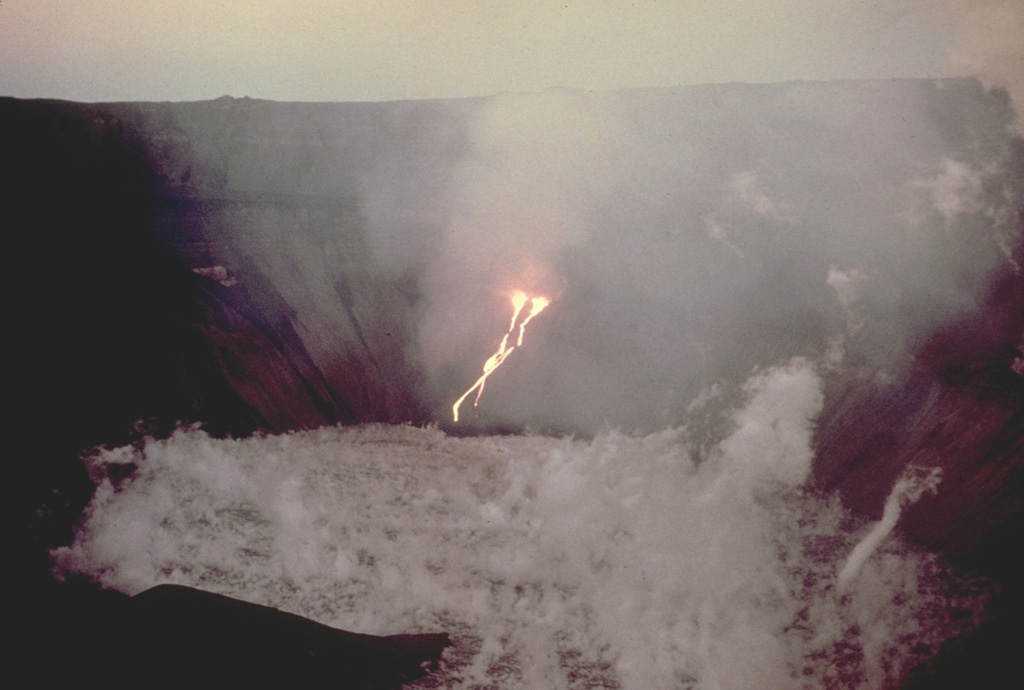Streams of incandescent lava descend into the steaming caldera lake of Fernandina volcano in December 1973.  This was one of several eruptions during the 1970's that produced lava flows from vents on caldera benches that spilled into the caldera lake.  This eruption began on December 9 from vents 220 m below the east end of the SE bench, producing lava flows that formed a small lava delta in the lake.  Glow was no longer visible the night of December 15, and ground observation on December 17 confirmed that the eruption had ceased.  Photo by Mike Harris, 1973 (courtesy of Tom Simkin, Smithsonian Institution).