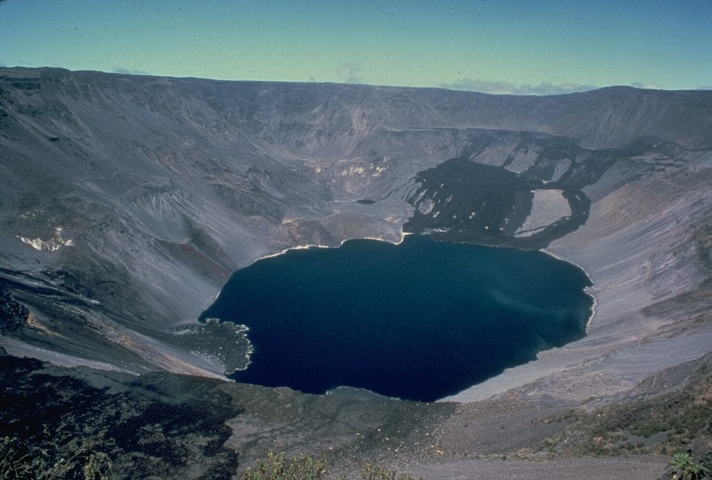 Fernandina, the most active of Galápagos volcanoes, is a basaltic shield volcano with a deep 4 x 6.5 km summit caldera.  This 1978 photo shows dark lava flows at the far NW end that were erupted from the NW caldera bench in August 1978.  The lava delta at the lower left was formed by lava flows down the west side of the SE bench in 1977.  In 1968 the caldera floor dropped 350 m following a major explosive eruption.  Collapse of part of the east caldera wall during a 1988 eruption produced a debris-avalanche deposit that absorbed the caldera lake. Photo by Chuck Wood, 1978 (Smithsonian Institution).