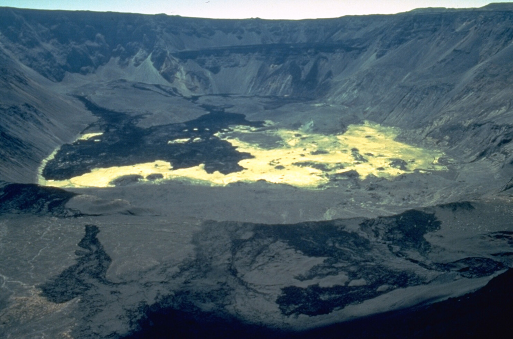 The light-colored lake sediments on the caldera floor are partially overlain by deposits of a massive debris avalanche produced when the east caldera wall collapsed on September 14, 1988.  The debris avalanche swept into the caldera lake, displacing it and initially raising its level over 100 m.  Lava flows from vents at about 750 m on the inner east wall were erupted through and onto the surface of the avalanche deposit on September 14-16, forming the dark areas at the left.  By the time of this January 1989 photo the lake had been largely absorbed within the avalanche deposit. Photo by Minard Hall, 1989 (Escuela Politécnica Nacional, Quito).