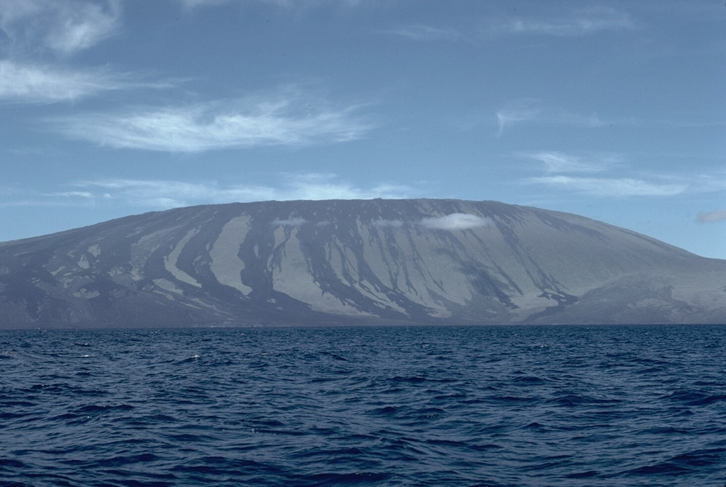 Wolf, the highest volcano of the Galápagos Islands, is located near the equator at the N end of the archipelago's largest island, Isabela. The summit caldera is 5.5 x 7 km and 600 m deep, with recent lava flows covering the broad caldera floor. Prominent unvegetated lava flows are visible on the flanks to the sea. Wolf's 1797 eruption was the first documented in the Galápagos Islands. Photo by Lee Siebert, 1978 (Smithsonian Institution).