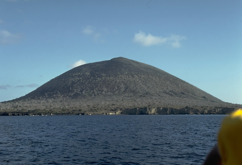 An unnamed 394-m-high cinder cone is a prominent landmark near James Bay at the western end of Santiago Island.  The eruptions that constructed the cone were initially submarine, producing palagonitic tuffs.  As the cone grew above sea level, subaerial explosions produced basaltic scoria that forms the upper part of the cone.  A similar, but smaller cone lies immediately to the SE, out of view to the right. Photo by Lee Siebert, 1978 (Smithsonian Institution).