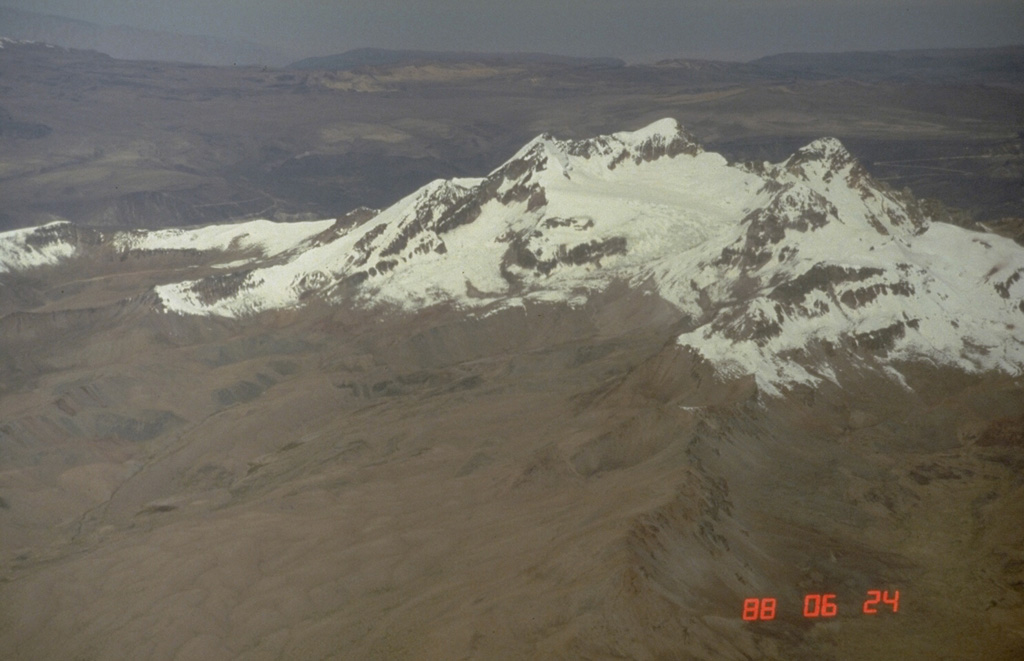 The glacier-covered Nevado Firura volcanic complex is seen here from the NW.  It consists of a 10-12 km long, NE-SW-trending cluster of small stratovolcanoes.  The highest peak is 5500-m Nevado Firura itself (right center).  Other volcanoes of the complex, including 5191-m-high Cerro Soncco Orcco, Cerro Jahsaya, and  Antapuna are located to the SW, left of this view.  Photo by Norm Banks, 1988 (U.S. Geological Survey).