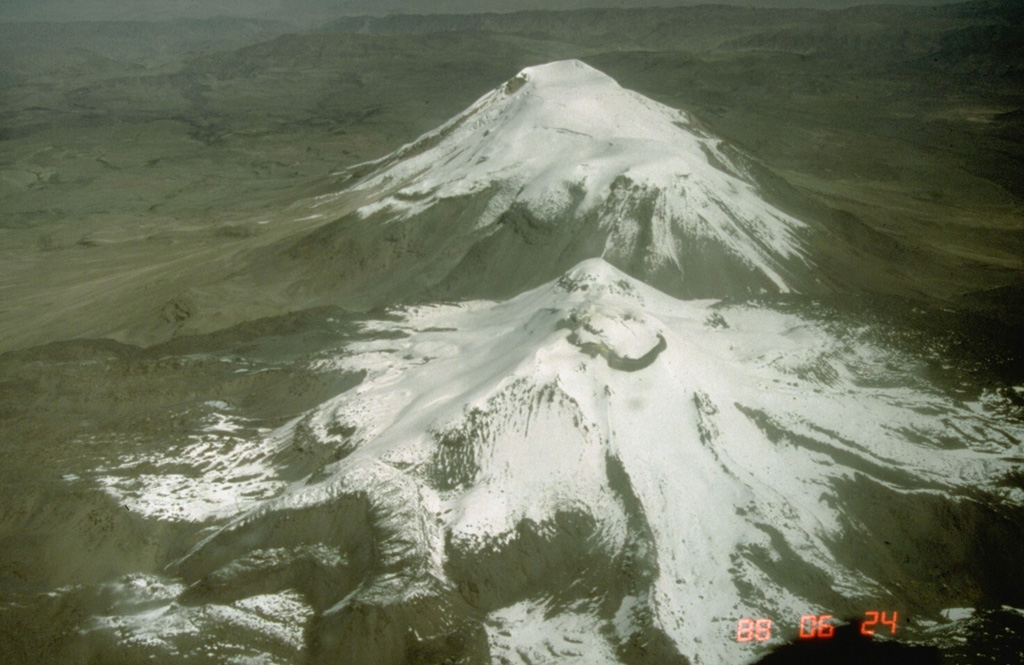 The Sabancaya volcanic complex consists of Sabancaya volcano proper (foreground), the older 6288-m-high Ampato volcano (background), and 6025-m Hualca Hualca volcano.  Sabancaya, viewed here from the NE, is constructed on the saddle between the two older volcanoes.  It is the youngest of the three Holocene volcanic centers and the only one to have erupted in historical time.  An extensive 15-km-wide apron of trachytic and dacitic lava flows surrounds the 5967-m-high volcano.  Records of historical eruptions date back to 1750. Photo by Norm Banks, 1988 (U.S. Geological Survey).