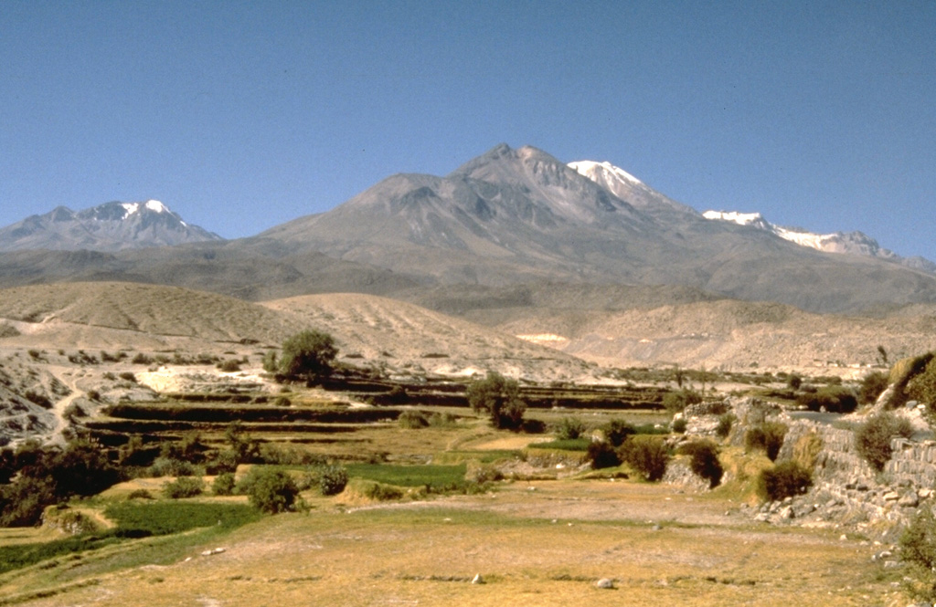 The Nevado de Chachani volcanic complex, seen here from the SW near the village of Yura, consists of a 360 km2 group of Pleistocene lava domes, a stratovolcano, and a shield volcano.  The central, 6057-m-high Nevado Chachani complex contains multiple vents along an arcuate line, including a well-defined summit crater at the western end.  Cerro La Horqueta (left horizon) may represent the latest activity from Nevado Chachani, after which activity migrated to the 8-km-wide Holocene lava shield of Pampa de Palacio on the south side. Photo by Norm Banks, 1988 (U.S. Geological Survey).