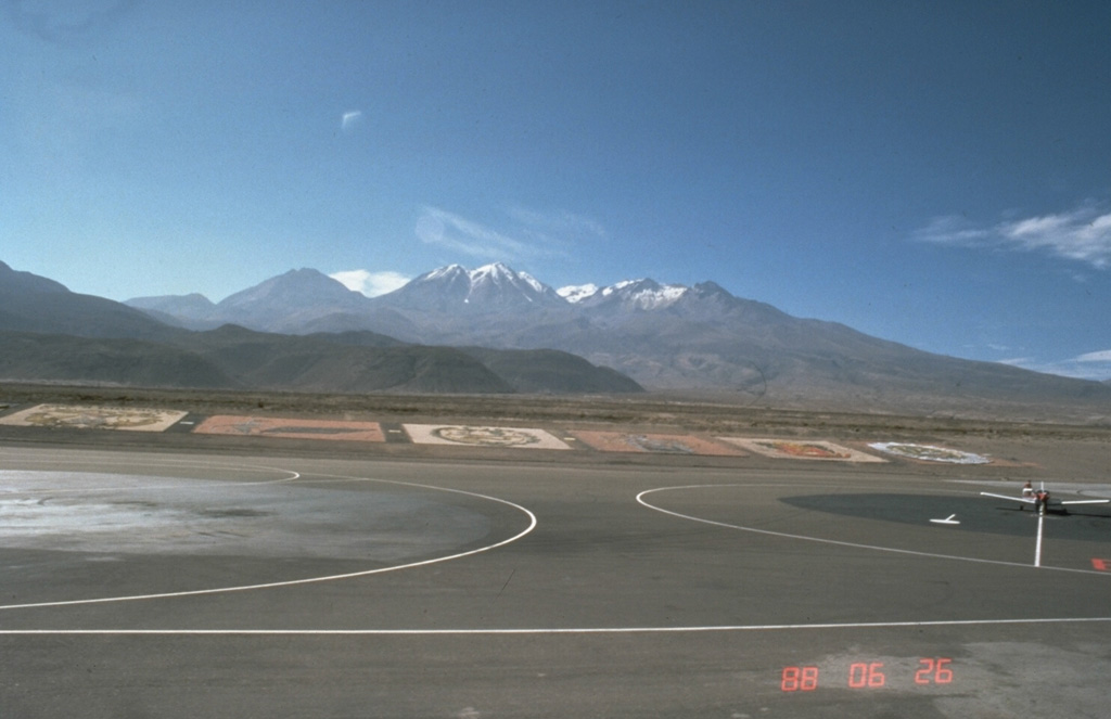 Nevado Chachani volcano towers north of the international airport at Arequipa, Perú.  The massive, 360 km2 volcanic complex includes a group of stratovolcanoes forming the horizon in this view, an older lava dome complex, and a younger SW-flank shield volcano.  The dark hills in the left-center foreground are the distal margins of viscous lava flows from the Pampa de Placio, the SW-flank shield volcano.  Volcanism has migrated to the west, and this marks the most recent activity of the Nevado Chachani complex.  Photo by Norm Banks, 1988 (U.S. Geological Survey).