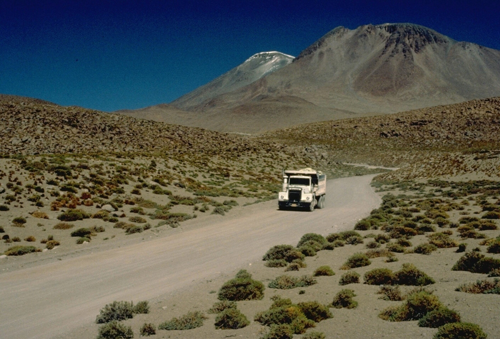 A truck bearing sulfur ore descends from Aucanquilcha volcano in northern Chile. The world's highest permanent human habitation is situated below a sulfur mine at the summit region of Aucanquilcha.  Several distinct cones were built on a 10-km-long, E-W-trending ridge forming the broad summit complex of the 6176-m-high stratovolcano, which is one of the largest in Chile.  Postglacial lava flows are visible on the upper flanks.  No historical eruptions are known from Cerro Aucanquilcha.  Copyrighted photo by Katia and Maurice Krafft, 1983.