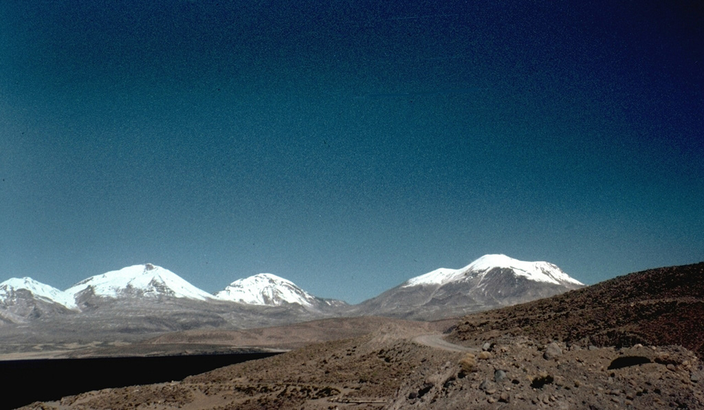 One of northern Chile's most active volcanoes, Volcán Guallatiri (right) is a symmetrical ice-clad stratovolcano at the SW end of the Nevados de Quimsachata volcano group.  This view from the west includes three other peaks of the Nevados de Quimsachata group at the extreme left, Pleistocene Volcán Humarata and Pleistocene-to-Holocene Volcán Acotango and Capurata volcano (center).  Minor explosive eruptions have occurred since the beginning of the 19th century from 6071-m-high Guallatiri volcano. Photo by Hugo Moreno (University of Chile).