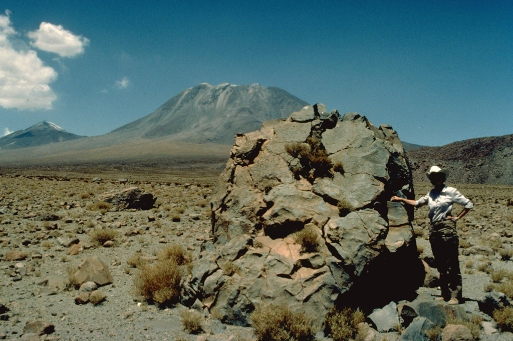 Collapse of the flow fronts of steep-sided andesitic-dacitic lava flows capping San Pedro volcano (background) produced an extensive apron of hot avalanche deposits that extends up to 20 km from the volcano.  Volcanologist Katia Krafft provides scale beside a prismatically jointed block in this view from the west.  The youngest cone of San Pedro was constructed within a scarp (whose northern wall forms the peak at the left) produced when an older edifice collapsed.  The 6145-m-high San Pedro forms a twin volcano with 6092-m San Pablo. Copyrighted photo by Katia and Maurice Krafft, 1983.